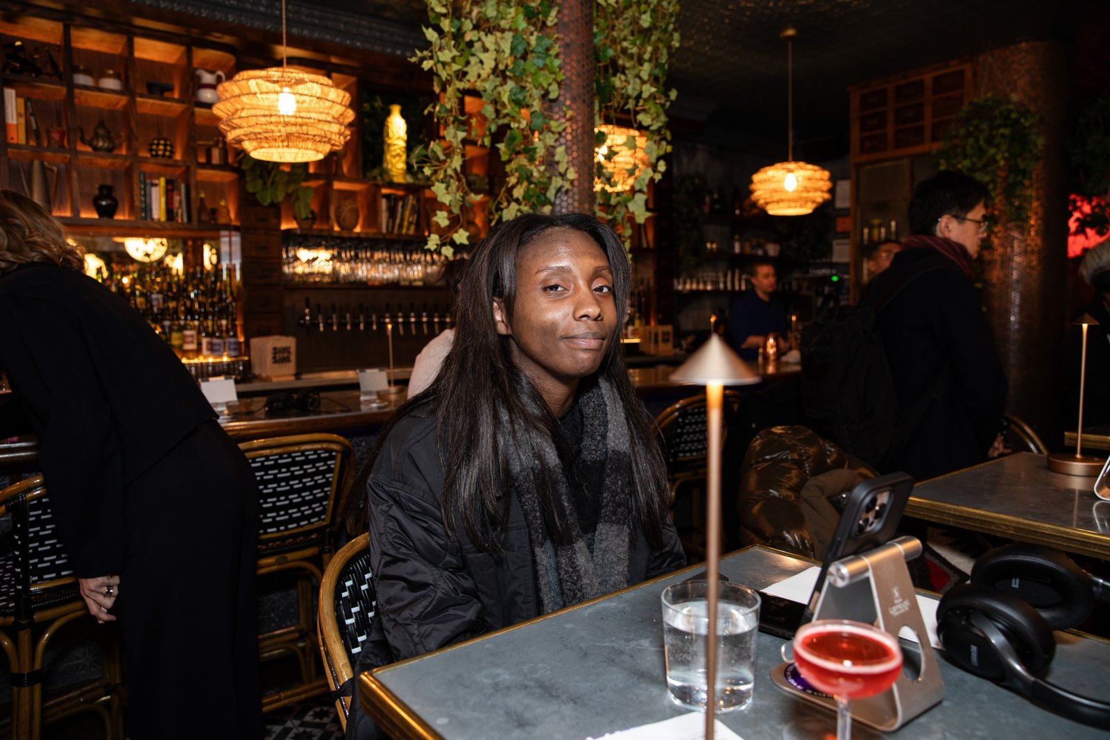 A Black woman in a black coat and scarf looks at the camera while at an AI dating cafe pop-up.
