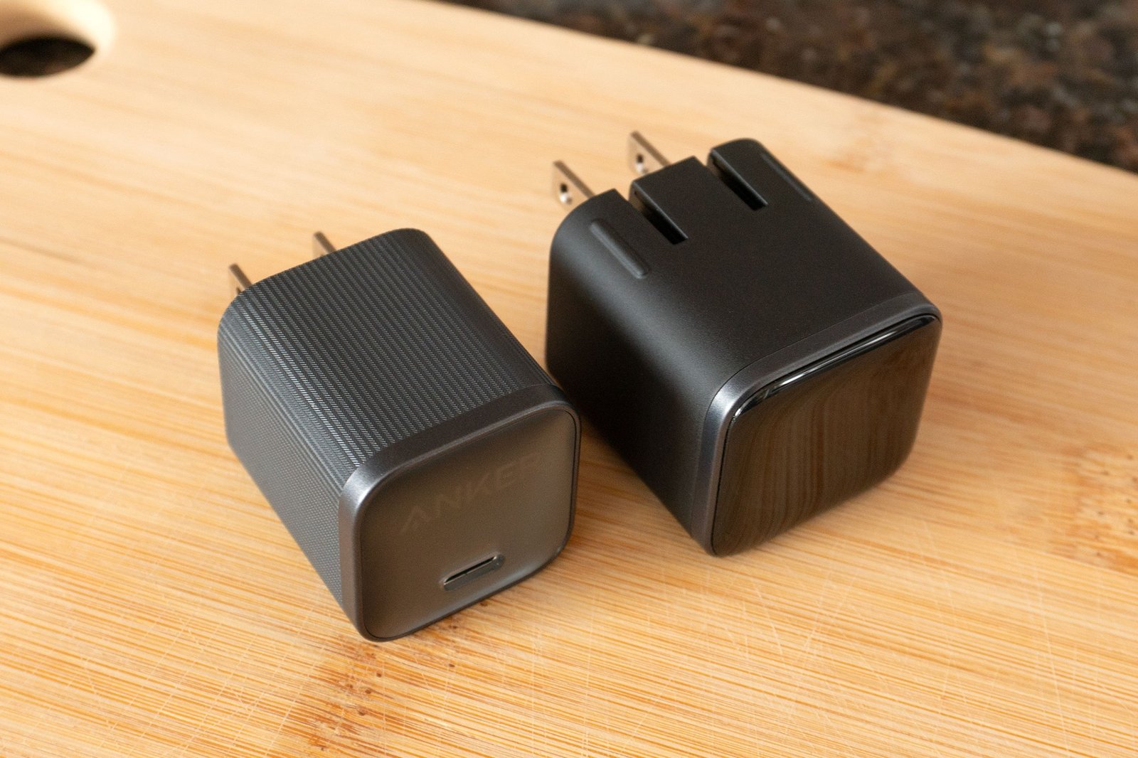 The new Anker Nano charger next to last year’s model on a wooden cutting board.