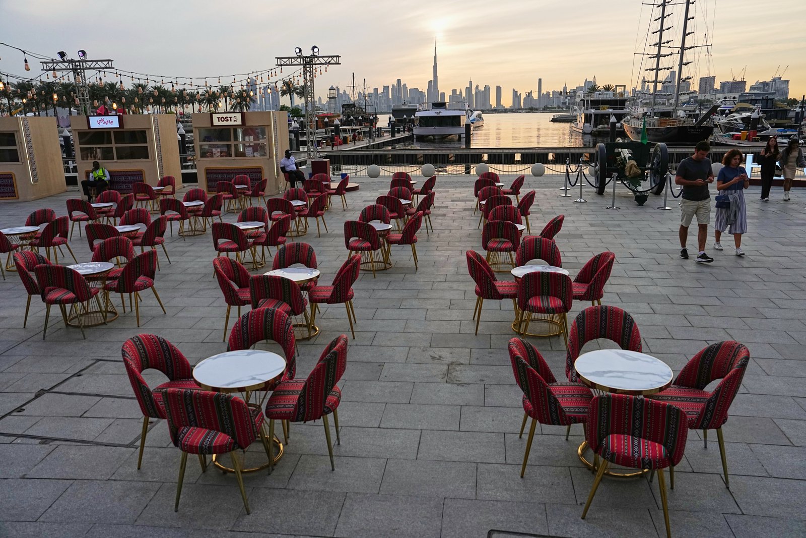 People walk past an outdoor empty restaurant at Dubai Creek Harbour