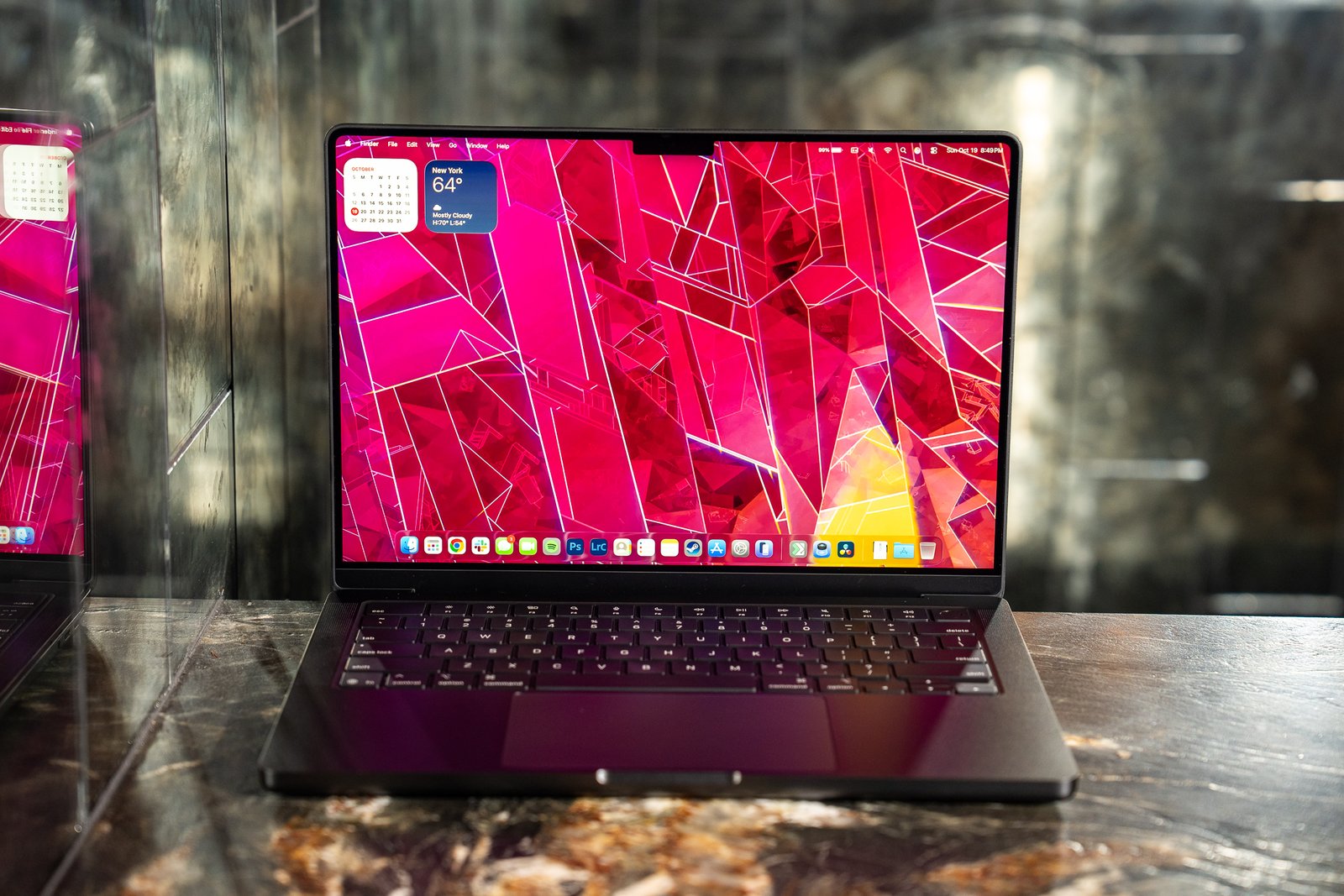 A 2025 14-inch MacBook Pro M5 on a marble bar top with a dark mirrored reflection behind it.