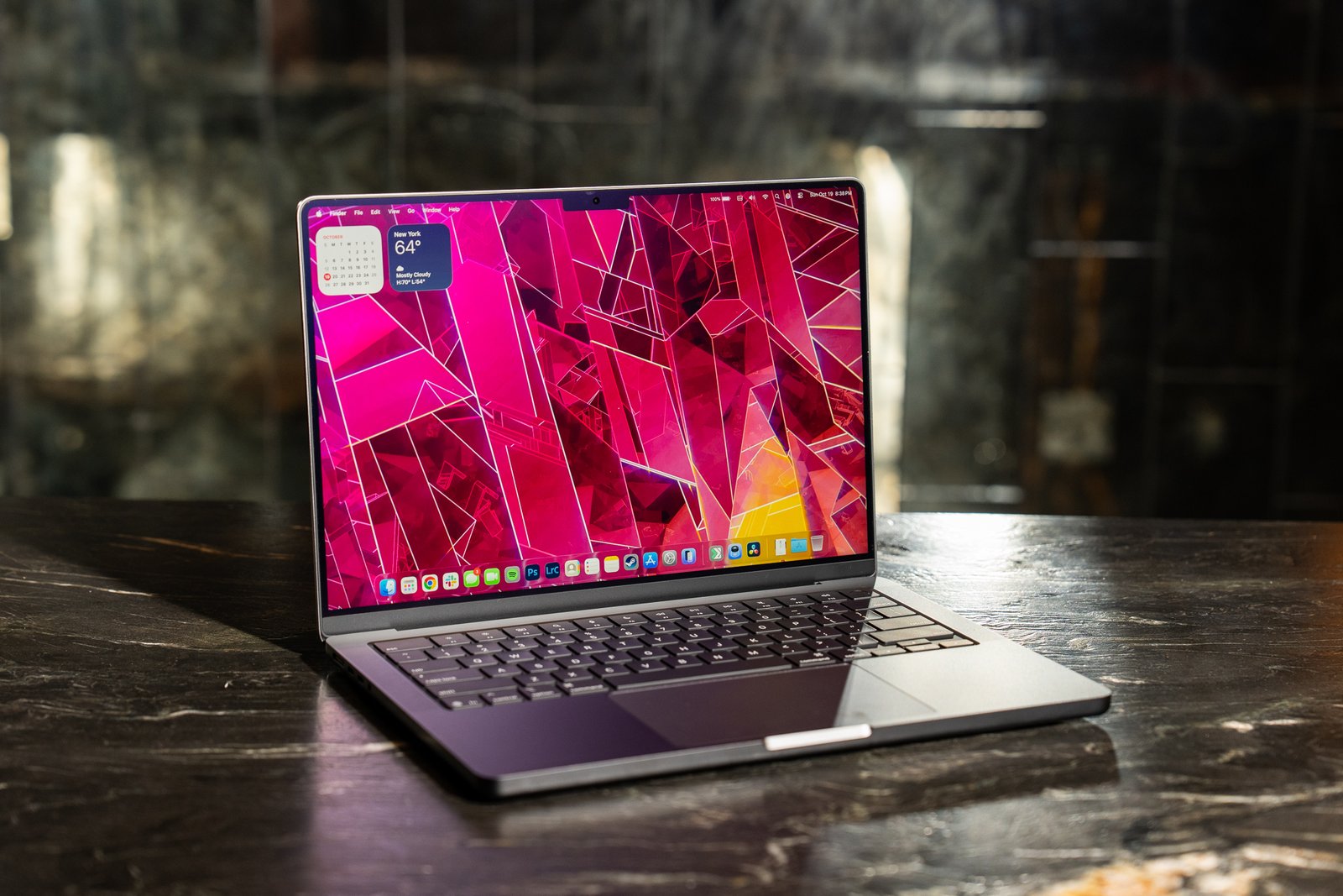 A 2025 14-inch MacBook Pro M5 on a marble bar top with a dark mirrored reflection behind it.