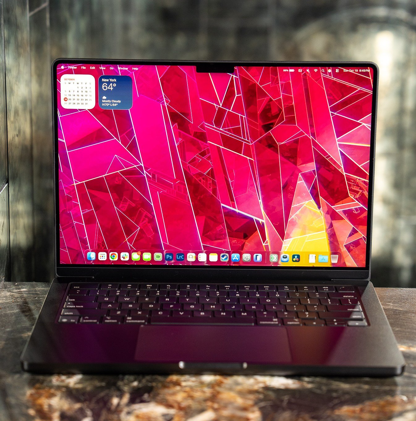 A 2025 14-inch MacBook Pro M5 on a marble bar top with a dark mirrored reflection behind it.