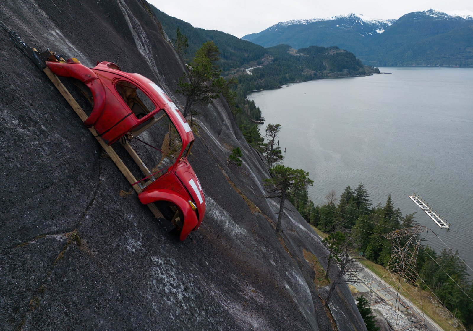 The shell of a Volkswagen Beetle hangs suspended on a cliff above the Sea-to-Sky Highway, in Squamish, British Columbia, Monday, April 6, 2026, after it appeared on the rock face last week with a large