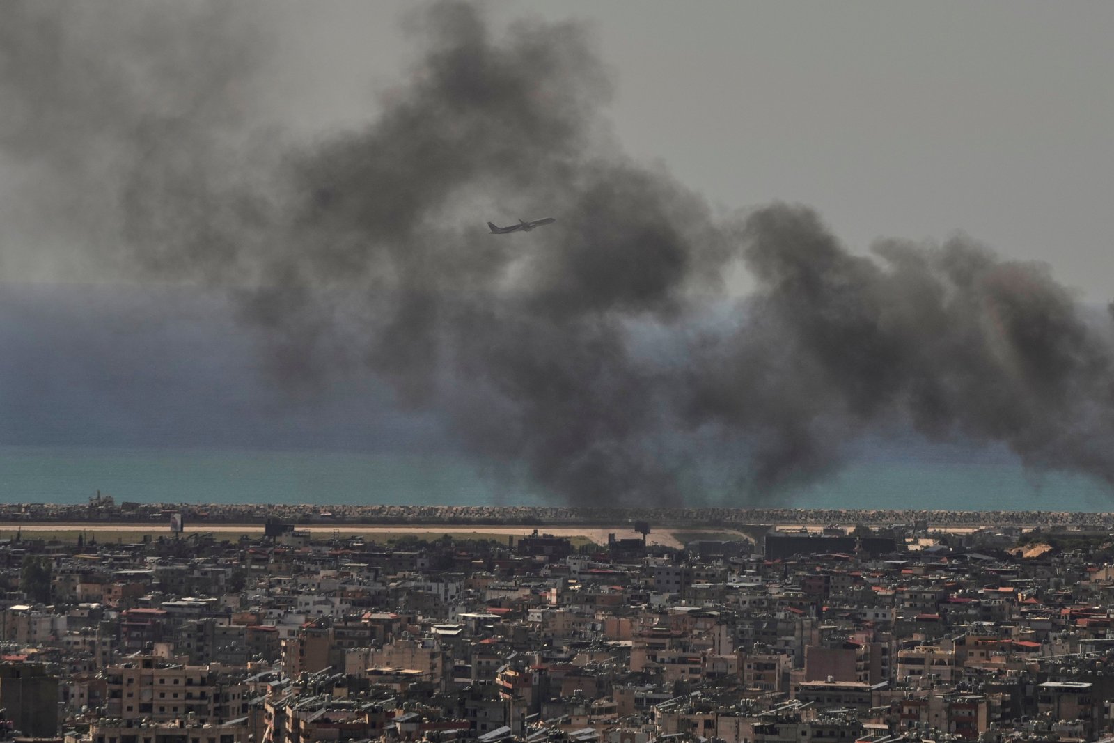 A Middle East Airlines plane takes off from Rafik Hariri International Airport as smoke rises from the site of an Israeli airstrike in Dahiyeh, Beirut's southern suburbs, Lebanon, Tuesday, March 17, 2026. (AP Photo/Hassan Ammar)
