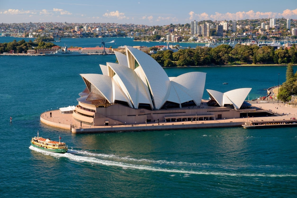 A bright day in Sydney, New South Wales, and this is the view from the Harbour Bridge looking across Sydney Harbour towards the iconic shape of the city's Opera House.